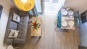 Une cuisine moderne avec un coin repas, un canapé agrémenté de coussins à motifs et une table basse en bois sur laquelle est disposé un arrangement floral rouge.