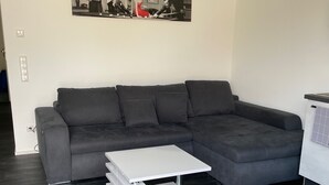 Ett modernt vardagsrum med en grå hörnsoffa, ett vitt soffbord och ett svartvitt konstverk på väggen.