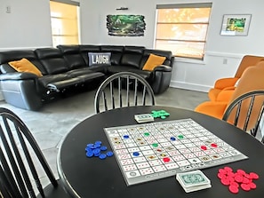 A living room with a black leather couch, a black table with a board game, and a window with blinds.