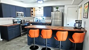 A modern kitchen with dark blue cabinets, stainless steel appliances, a wooden island with bar stools, and a hexagonal tile floor. - Family & Pet-Friendly River Escape w/ Kayaks, Manatees & Outdoor Fun! (Weeki Wachee)