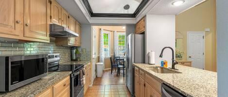 A kitchen with wooden cabinets, a granite countertop, a stainless steel refrigerator, and a dishwasher.