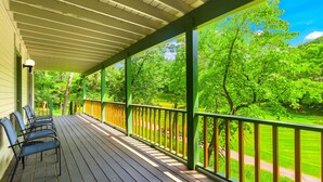 A covered porch with wooden flooring and green railings, overlooking a well-maintained lawn and trees. - "The Mint" @ Margaritaville Lake Resort, Boating, Golfing, Fire Pit, Swimming (Osage Beach)