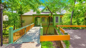 A green house with a porch, a wooden fence, and a paved walkway. - "The Mint" @ Margaritaville Lake Resort, Boating, Golfing, Fire Pit, Swimming (Osage Beach)