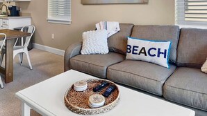 A living room with a beige sofa, a white coffee table, and a painting of a boat on the wall. - Two Minutes to Beach. Includes Taxi Bikes, Lake View, and Community Pool (Santa Rosa Beach)
