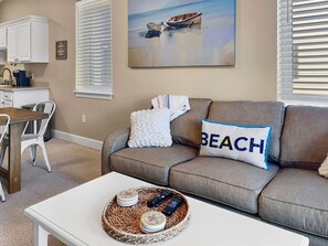 A living room with a beige sofa, a white coffee table, and a painting of a boat on the wall.