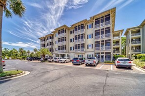 A multi-story hotel with balconies, a parking lot, and palm trees.