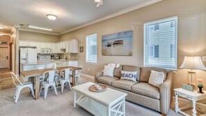 A spacious living room with a beige sofa, a dining table with chairs, and a kitchen in the background. - Two Minutes to Beach. Includes Taxi Bikes, Lake View, and Community Pool (Santa Rosa Beach)