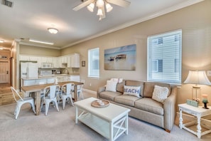 A spacious living room with a beige sofa, a dining table with chairs, and a kitchen in the background.