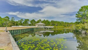 A tranquil lake with lily pads, a wooden dock, and a gazebo-like structure. - Two Minutes to Beach. Includes Taxi Bikes, Lake View, and Community Pool (Santa Rosa Beach)