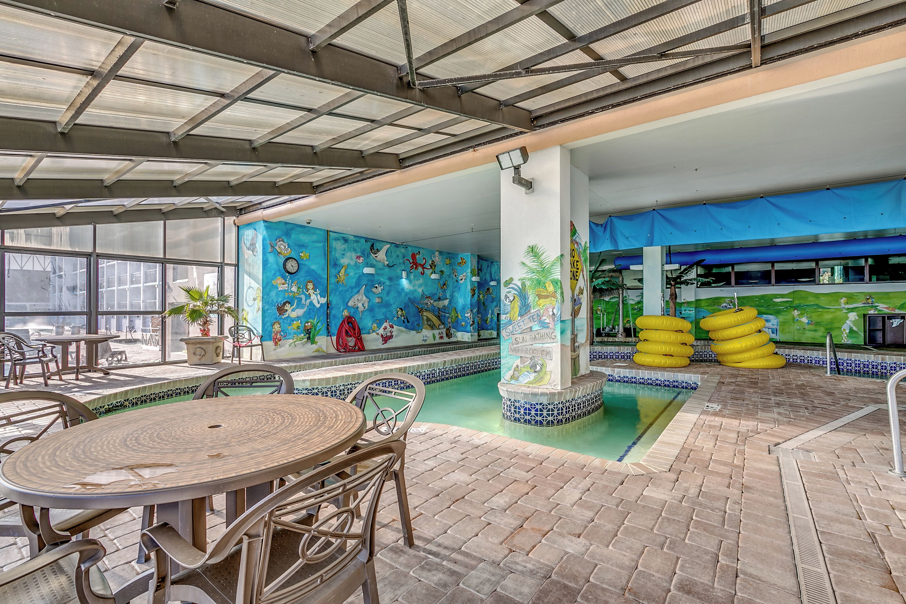 Zona de piscina interior con un mural, asientos y flotadores inflables.