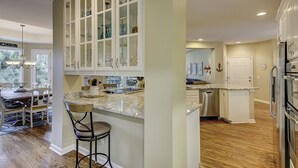 A kitchen with white cabinets, a marble countertop, and a stainless steel refrigerator. - 10 Heath - Breathtaking Fazio Golf Course Views (Hilton Head Island)