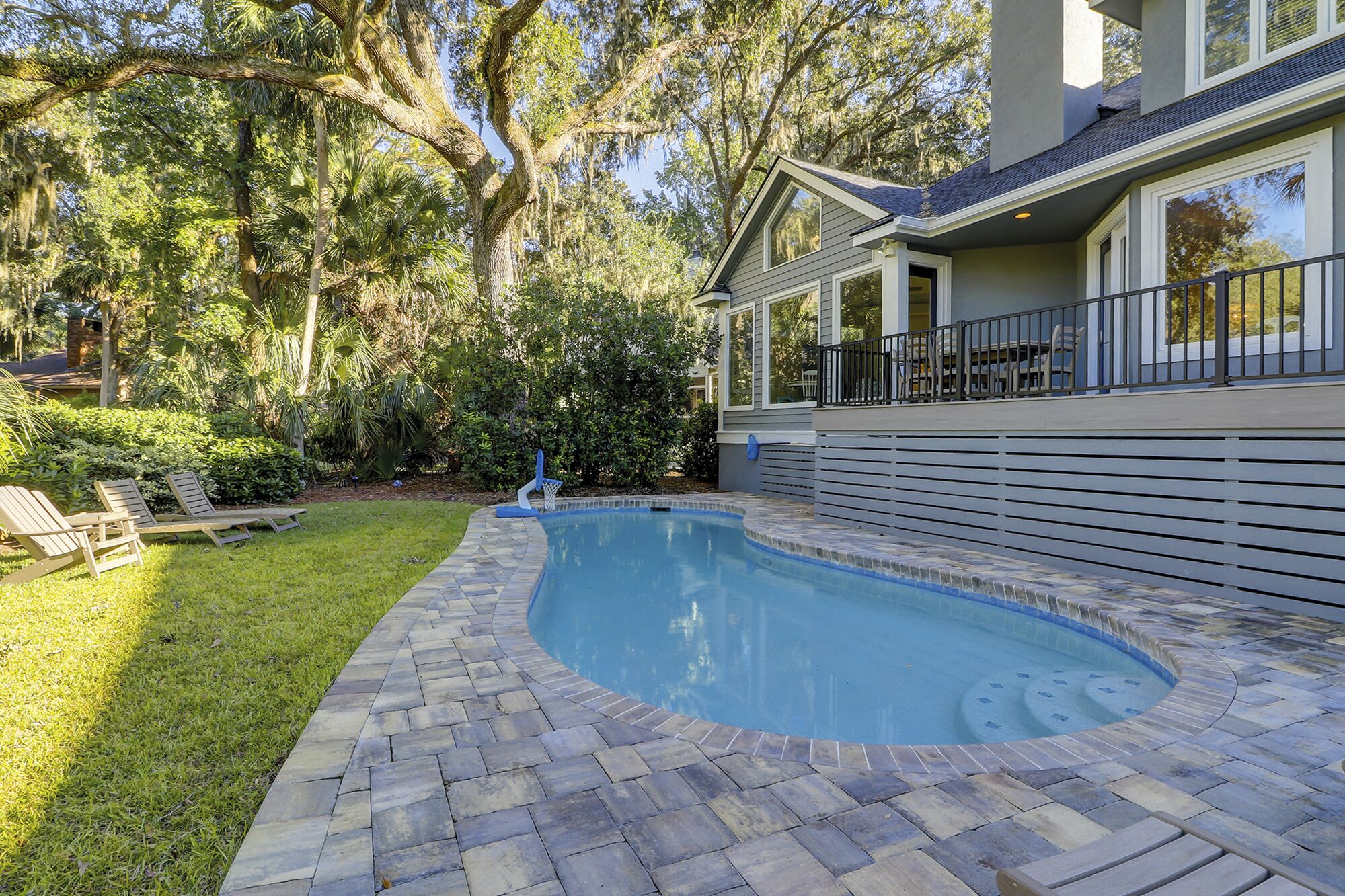 A swimming pool with a stone deck, surrounded by a well-maintained lawn and trees.