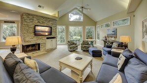 A spacious living room with a stone fireplace, comfortable seating, large windows, and artwork on the walls. - 10 Heath - Breathtaking Fazio Golf Course Views (Hilton Head Island)