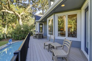 Une terrasse extérieure couverte avec une piscine, des meubles en bois et de grandes fenêtres donnant sur un jardin luxuriant.