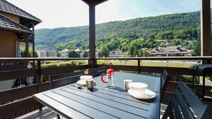 A balcony with a table set for two, overlooking a forested hillside.
