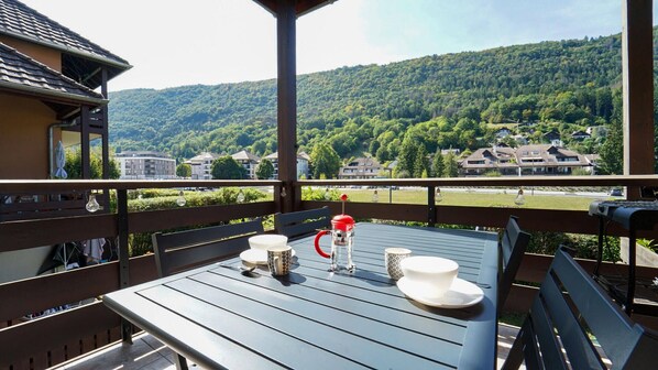 Een balkon met een tafel voor twee personen, met uitzicht op een beboste heuvel.