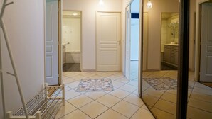 A hallway with a white door, a small bathroom with a shower, and a tiled floor.
