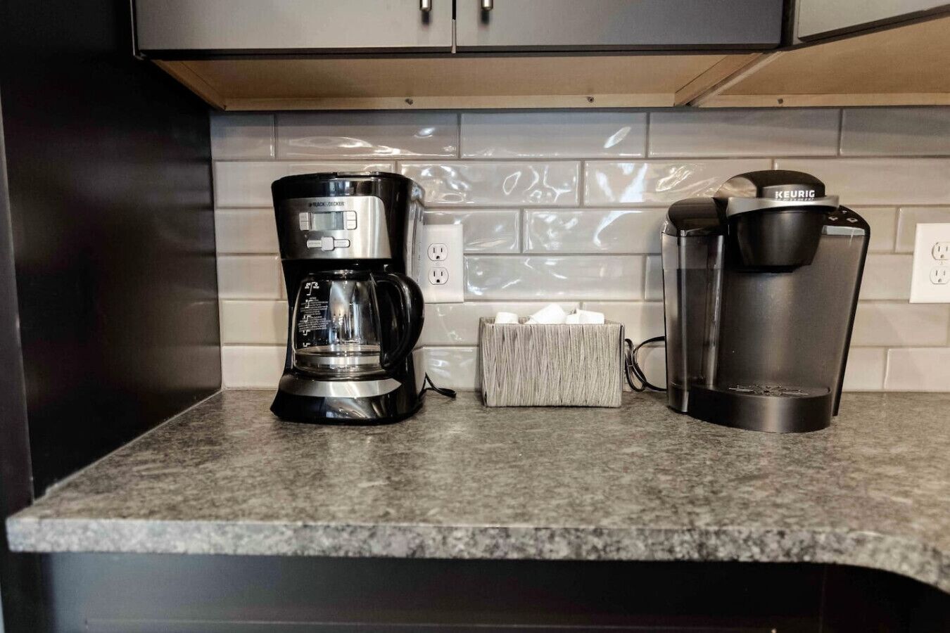Una cocina con cafetera, una Keurig y un portalapices para cápsulas de café sobre la encimera.