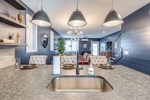 Una cocina moderna con un lavamanos integrado, tres lámparas colgantes y un comedor con sofá y mesa para cuatro.