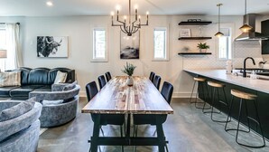 Una cocina moderna con una mesa de comedor de madera, taburetes negros y lámparas colgantes.
