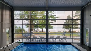 An indoor swimming pool with a view of the outdoors, surrounded by metal railings and a covered patio area.