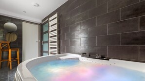 A modern bathroom with a freestanding bathtub, dark tiled walls, a wooden chair, and a mirror. - Grand Chalet Standing Avec Jacuzzi à Chamrousse ski 1750 (Chamrousse)