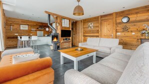A modern living room with a fireplace, wooden walls, a sofa, and a dining area. - Grand Chalet Standing Avec Jacuzzi à Chamrousse ski 1750 (Chamrousse)