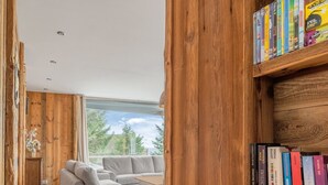 A modern living room with a grey sofa, wooden walls, and a bookshelf filled with books. - Grand Chalet Standing Avec Jacuzzi à Chamrousse ski 1750 (Chamrousse)