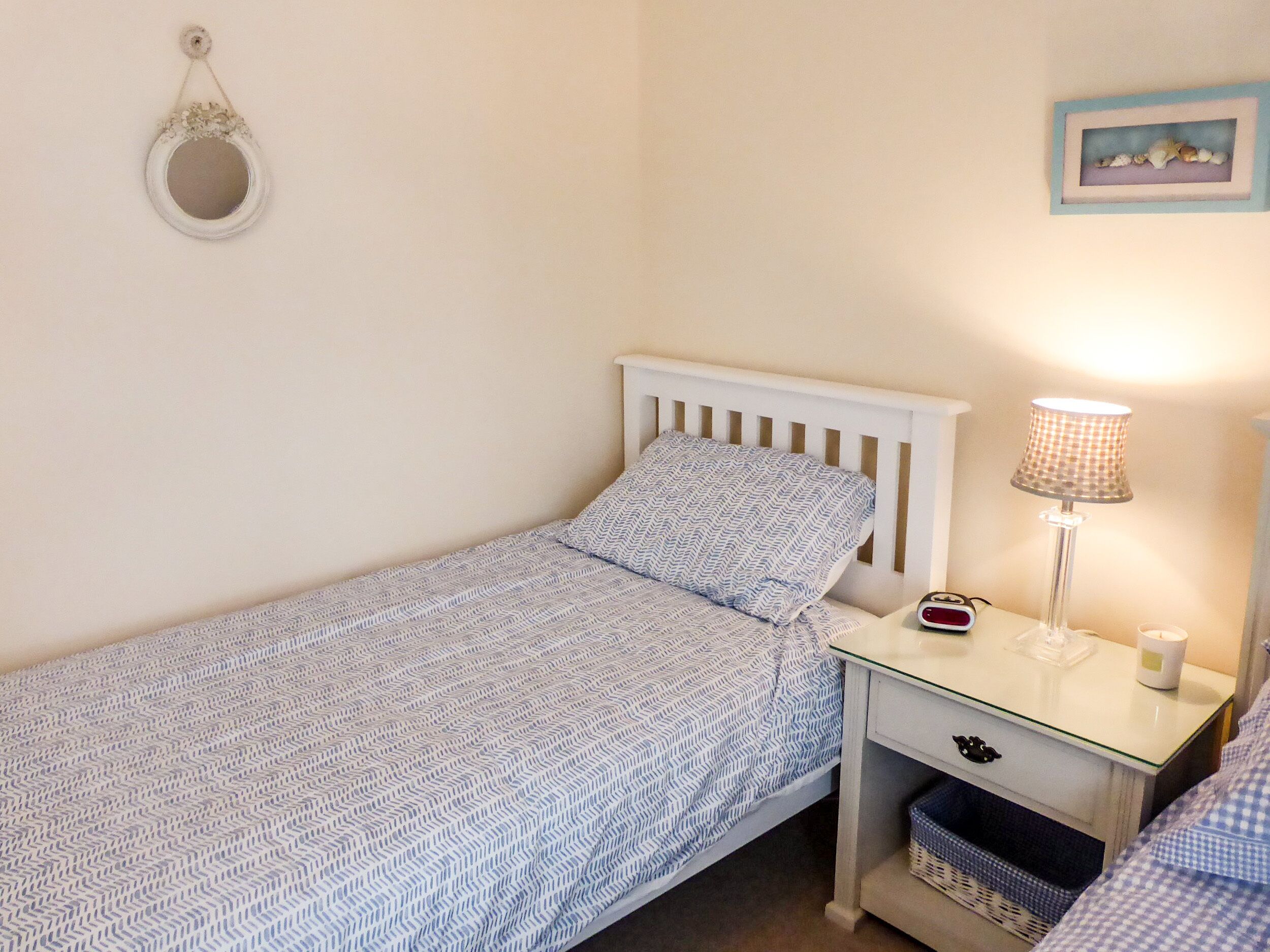 Een compacte, verzorgde slaapkamer met een enkel bed, een nachtkastje met een lamp en een spiegel aan de muur.