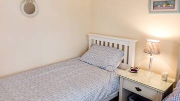 Een compacte, verzorgde slaapkamer met een enkel bed, een nachtkastje met een lamp en een spiegel aan de muur.