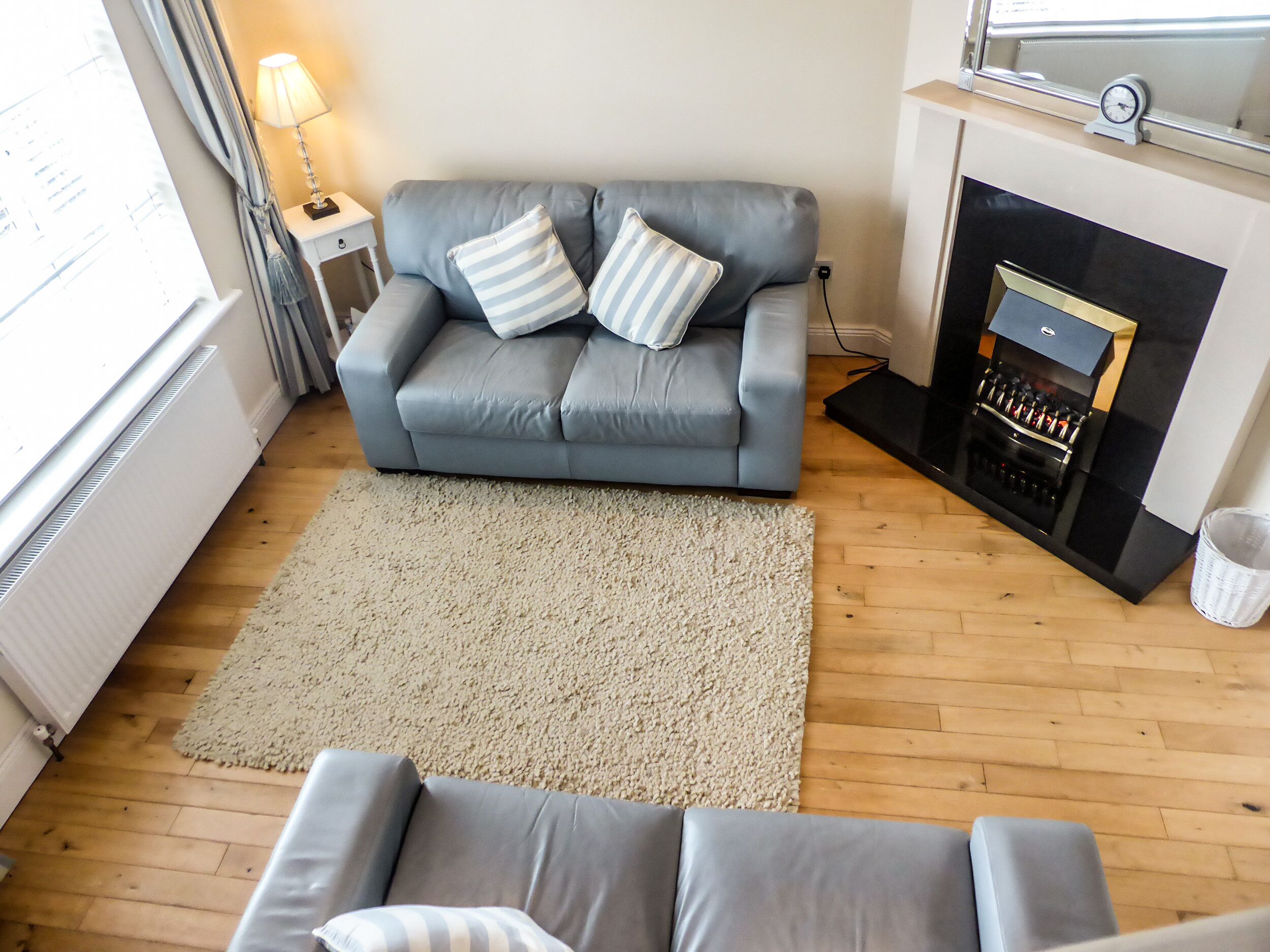 Un salon avec un canapé gris, un tapis blanc et une cheminée.
