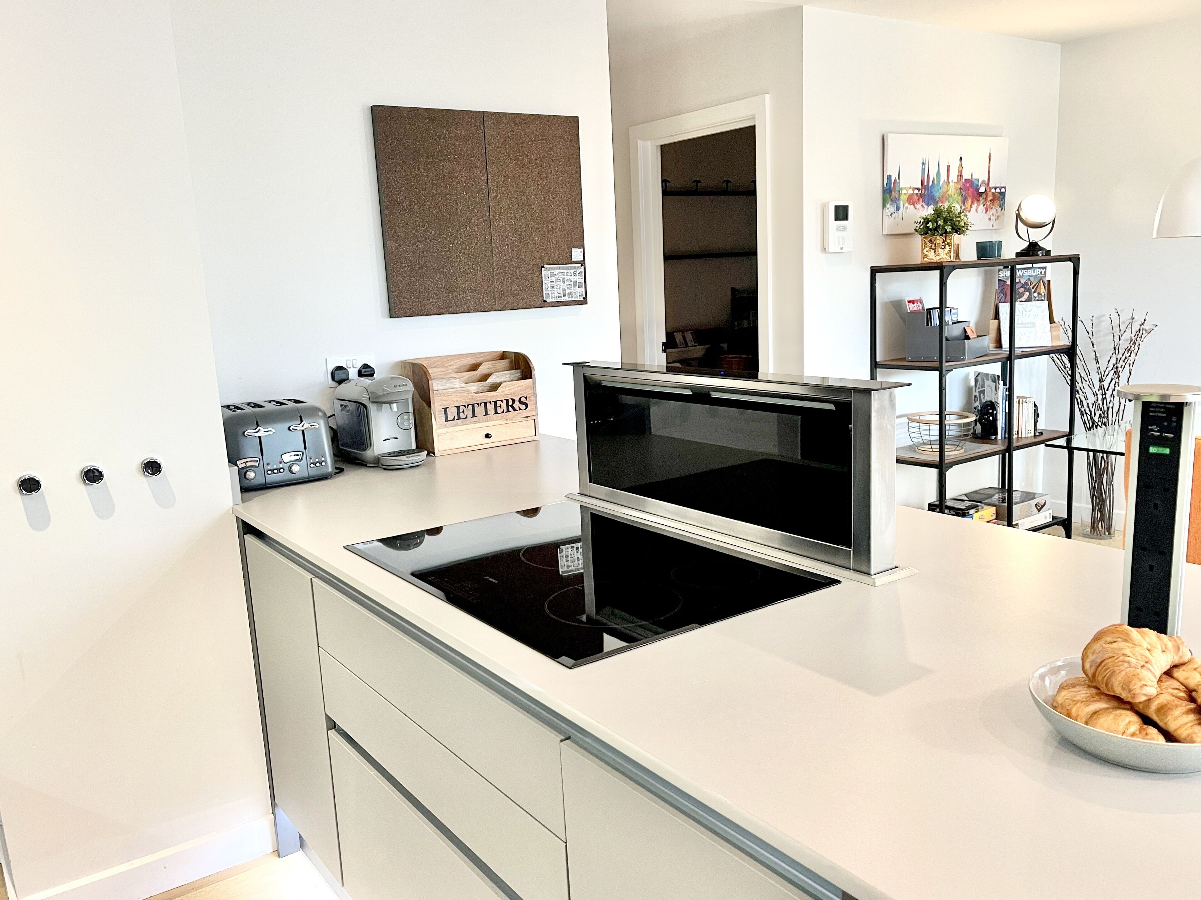 A modern kitchen with a built-in oven, a coffee maker, and a bowl of croissants.