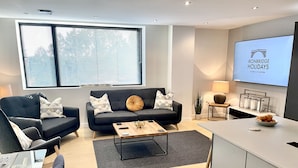 A modern living room with a sofa, coffee table, and a TV displaying 'Ironbridge Holidays'. - Apartment Twelve (Shrewsbury)