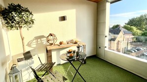 A balcony with a small table, a potted plant, and a view of buildings. - Apartment Twelve (Shrewsbury)