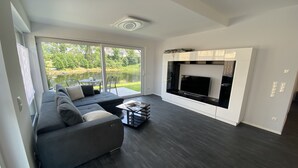 A modern living room with a dark wood floor, a grey sectional sofa, a glass coffee table, and a fireplace. - Apartments-Saaldorf WG1 with terrace and view of the reservoir (Bad Lobenstein)