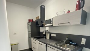 A modern kitchen with white cabinets, a stainless steel sink, and a microwave. - Apartments-Saaldorf WG1 with terrace and view of the reservoir (Bad Lobenstein)