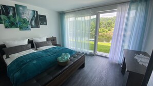 A bedroom with a bed, a bench, a desk, and a view of a garden through a sliding glass door. - Apartments-Saaldorf WG1 with terrace and view of the reservoir (Bad Lobenstein)