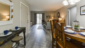 Uma sala de jantar com uma mesa de madeira posta para quatro pessoas, um banco de madeira escura e um lustre.