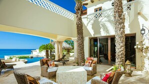 Een luxe terras buiten met rieten meubels, een zwembad en uitzicht op de oceaan.