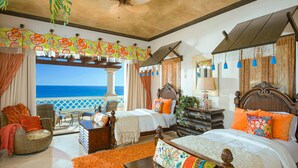 Een slaapkamer met een groot bed, een kleiner bed en een zithoek met uitzicht op de oceaan.