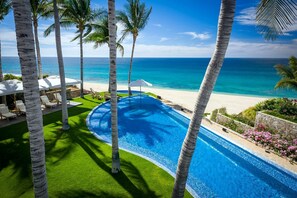Ein Pool mit Blick auf das Meer, umgeben von Palmen und Liegestühlen.