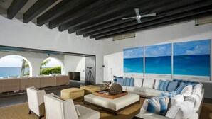 A spacious living room with a large window overlooking the ocean, a fireplace, and a modern ceiling design. - Luxurious 7 BR Beachfront Casa Oliver w/ WiFi, Pool, Home Theatre, Gym + More! (San Jose del Cabo)