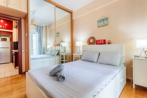 A hotel room with a bed, bedside tables, a mirror, a kitchenette, and a view of the outside. - Athens Strawberry Hideaway - City Cozy Gem (Athina)