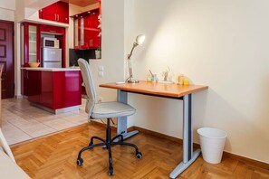 A compact kitchen with red cabinets, a microwave, and a small dining area with a desk and chair.