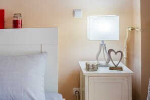 Une table de chevet bien rangée, avec une lampe, un objet décoratif en forme de cœur et un petit récipient en verre.