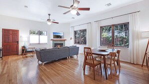 A spacious living room with hardwood flooring, a gray sofa, a dining table with chairs, and two ceiling fans. - Venice Beach Cottage with incredible outdoor space!! (Venice)