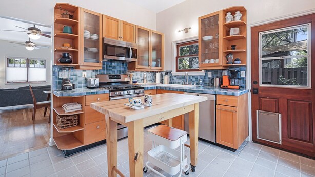 A modern kitchen with wooden cabinets, a central island, and a dining area with a chair and table. - Venice Beach Cottage with incredible outdoor space!! (Venice)