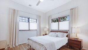A bedroom with a bed, two bedside tables, a ceiling fan, and windows with curtains. - Venice Beach Cottage with incredible outdoor space!! (Venice)