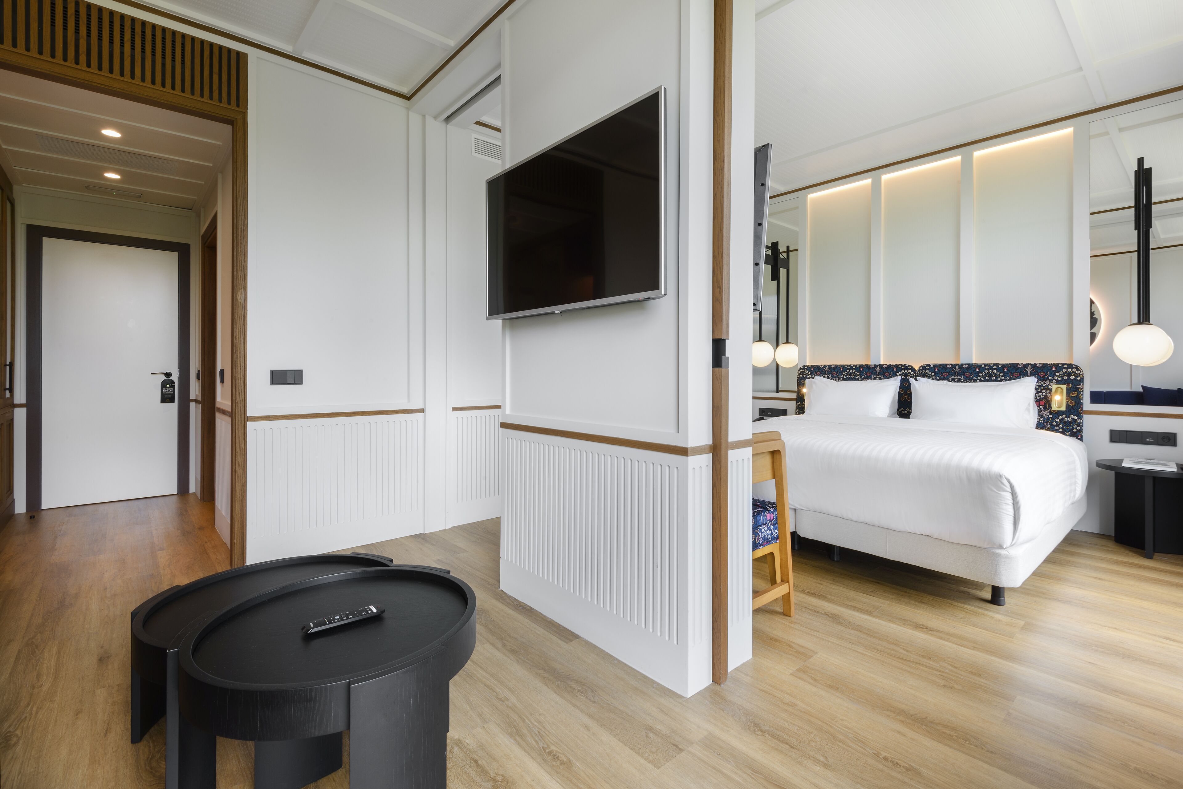 Una habitación de hotel moderna con una cama grande, un televisor de pantalla plana en la pared, una mesita y una silla.