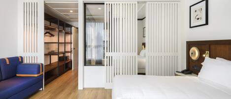 A hotel room with a bed, a blue sofa, a wardrobe, and a mirror.